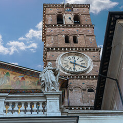 a fragment of the facade of a Roman cathedral with a beautiful tower clock and a statue of a saint against the blue sky