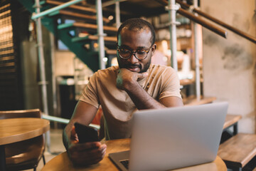 Skilled freelance copywriter using cellphone and laptop for sharing media files via bluetooth...