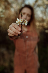 Blurred portrait of female model with blossomed tree flower in arm. Woman giving flower in to camera 