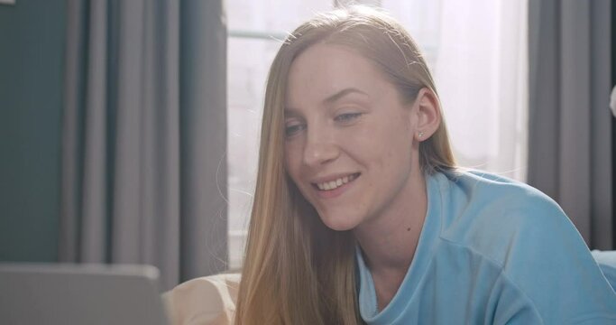 Portrait of young caucasian woman styding in her bedroom. Pretty female lying on bed and using laptop notebook to work.