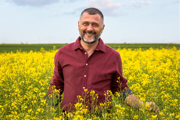 Naklejka na ściany i meble Portrait of smiling middle age farmer standing in rapeseed field examining crop.