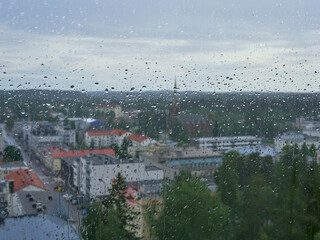 Panorama of European city in the rain: blurred picture of drop on glass.