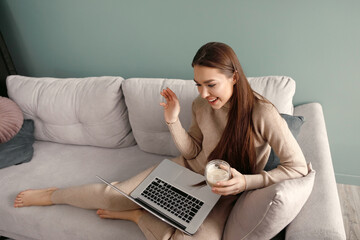 Happy woman at home using laptop sitting on sofa, online working at home.