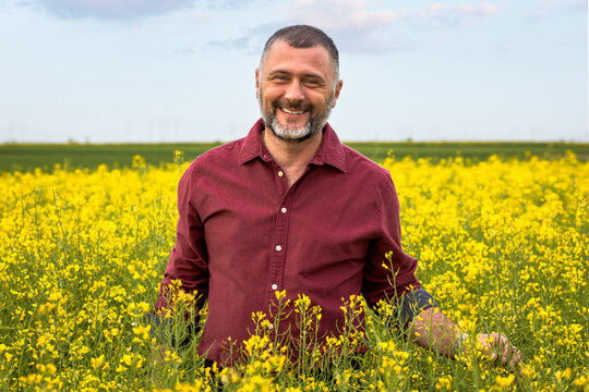 Portrait of smiling middle age farmer standing in rapeseed field examining crop. - Powered by Adobe