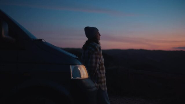 Cinematic lens view, soft blurry focus on young lonely woman, traveler watching colorful stunning Porto sunset, leaning on adventurous camper van, dreaming about happy carefree future life near ocean