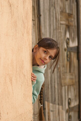 A girl peeks out around the corner. A little girl (nine years old) spies on someone and peers around the corner. Outdoors