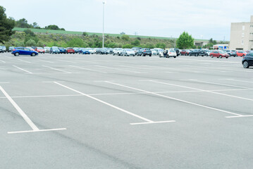 Parking area for cars with white painted lines with free spaces in the foreground and in the background out of focus many cars parked in the background