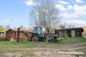 Old abandoned tractor on the background of barns