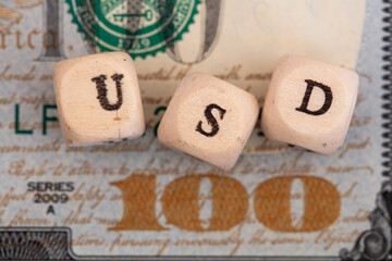 USD word written on wooden blocks on 100 dollar banknote background