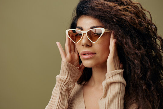 STYLISH EYEWEAR CONCEPT. Happy adorable tanned curly Latin female in casual things wear trendy sunglasses posing isolated over olive green background. Copy space Mockup Banner. Fashion closeup offer