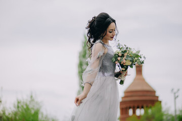 Fototapeta na wymiar Side view of adorable bridesmaid in front of the church, holding bridal bouquet and looking down