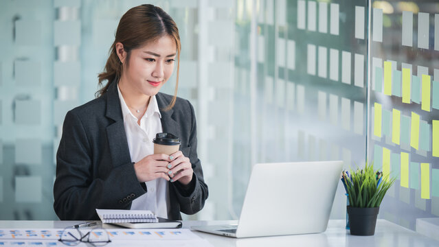 Portrait of an Asian woman holding a coffee cup Working on a tablet computer in a modern office Make an account analysis report. real estate investment information financial and tax system concepts