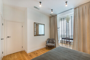 The interior of a bedroom with a panoramic window, a mirror on a light wall and a table with a chair by the window.