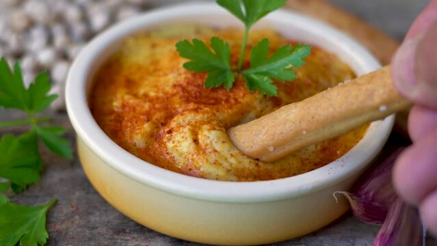Slow motion, bread stick spreading natural chickpea hummus.
