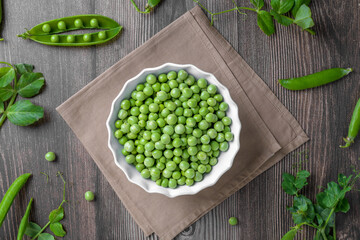 Fresh organic raw green peas in a bowl with peas plants leaves on dark wooden table background. Healthy eating, vegan and vegetarian legume food, raw food and detox super food, bean protein, top view