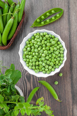 Fresh organic raw green peas in a bowl with peas plants leaves on dark wooden table background. Healthy eating, vegan and vegetarian legume food, raw food and detox super food, bean protein, top view