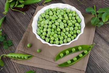 Fresh organic raw green peas in a bowl with peas plants leaves on dark wooden table background. Healthy eating, vegan and vegetarian legume food, raw food and detox super food, bean protein, close up
