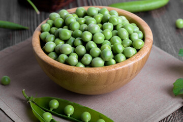 Fresh organic raw green peas in a bowl with peas plants leaves on dark wooden table background. Healthy eating, vegan and vegetarian legume food, raw food and detox super food, bean protein, close up