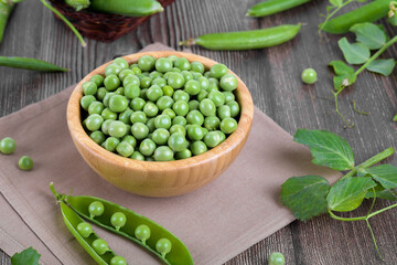 Fresh organic raw green peas in a bowl with peas plants leaves on dark wooden table background. Healthy eating, vegan and vegetarian legume food, raw food and detox super food, bean protein, close up
