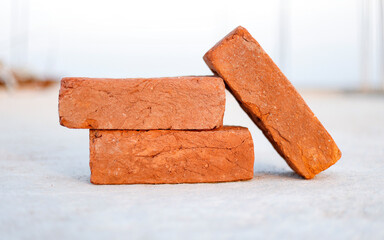 3 orange Bricks on a Cement Floor, Used for Construction of a house in India. These bricks are made by soil by heating them.