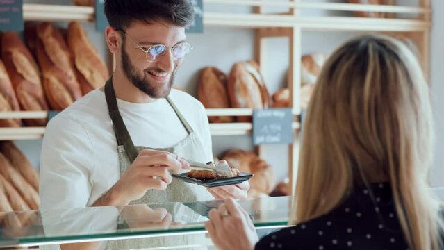 Video of smiling man seller giving fresh chocolate croissants to cheerful woman in the pastry shop.