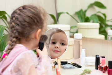 Obraz na płótnie Canvas Happy little cute girl playing with her mother's cosmetic, selfcare, beauty procedure Treatment, makeup, visage, powdering face in front of mirror at home.