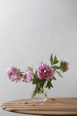 Pastel pink peony flowers bouquet in a glass vase on wooden table. 
