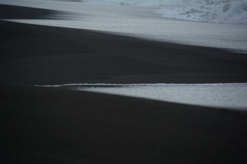 Receding Wave on the black sand beach forms different shapes in the sand with every wave coming in. The black sand beach by the Pacific Ocean in Guatemala is caused by the many Volcanos.