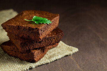 brownie cake. Dark chocolate brownie on the sackcloth. stack of chocolate brownies on wooden background with green mint leaf on top, homemade bakery and dessert with copy space.