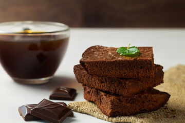 Stack of chocolate brownies on white background with green mint leaf on top. Dark chocolate brownie with pieces chocolate on the sackcloth. Homemade bakery and dessert with copy space.