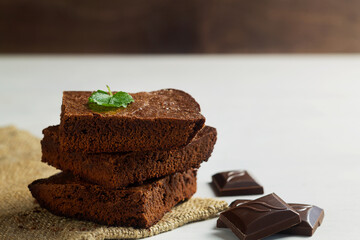 brownie cake. Stack of chocolate brownies on white table with green mint leaf on top. Dark chocolate brownie with pieces chocolate on the sackcloth. Homemade bakery and dessert with copy space.