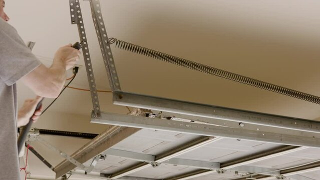A homeowner or handyman type removing the old spring from a garage door automatic opener system.