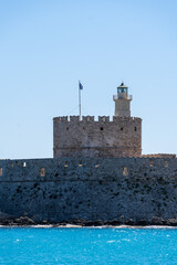 Saint Nicholas Fortress in Mandraki Harbor in focus and Seaside chair at day time.