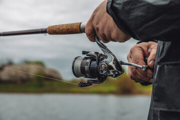 Fishing rod with a spinning reel in the hands of a fisherman on an overcast spring day. Fishing...