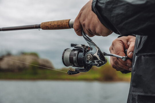 Fishing rod with a spinning reel in the hands of a fisherman on an overcast spring day. Fishing background.