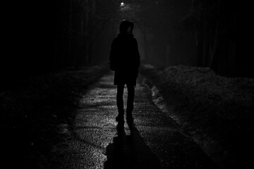 Silhouette of man at night in park. Man walks alone on road in evening.