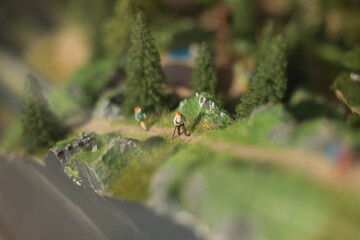 Tourists go uphill in summer. Hiking. Toy figures of people on model of mountainous area.