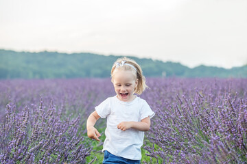 Little girl runs in lavender field. Beautiful joyful blond toddler girl. Cheerful kid