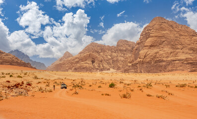 Fototapeta na wymiar Orange sands and cliffs of Wadi Rum desert with tourist car in the background, Jordan