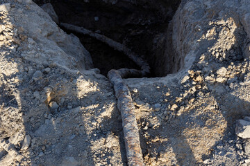 A rusty old telecommunications cable, dug into the ground. Top view.