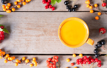 Seasonal healing sea buckthorn rose hip viburnum rowan berry herbal tea in clay cup on wooden table