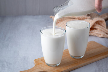 Pouring homemade kefir, buttermilk or yogurt with probiotics. Yogurt flowing from glass bottle on light background. Probiotic cold fermented dairy drink. Trendy food and drink. Copy space