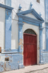 Red wooden door of a church in Campeche, Mexico. Weathered and aged facade with fainted paint. 