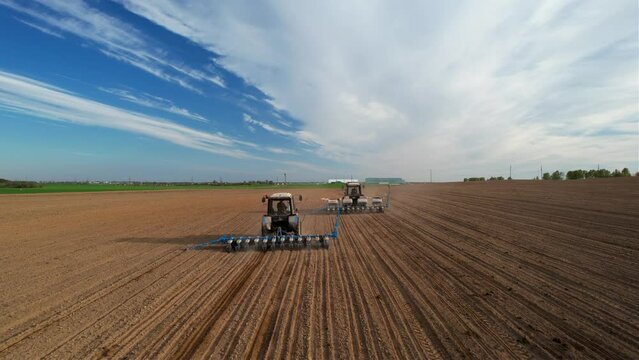 Tractor sowing seed on plowed field, drone view. Seeding machinery for plowing field. Seed sowing and soil cultivating.Tractor with disk harrow on plowing field. Ploughing and seeding with tractors.

