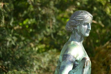 In the green city park in the middle of the pond a stone figure of a woman