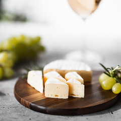 Camembert cheese on a wooden board. In the background a glass of wine.