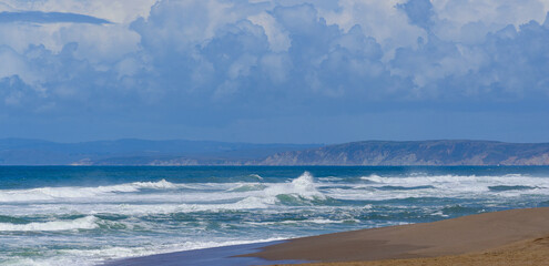 Fototapeta na wymiar Crashing surf cresting waves on a beautiful Pacific Ocean beach with the bright blue sky