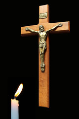 Lit candle ahead of wooden cross with body of Christ - obrazy, fototapety, plakaty