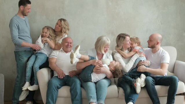 Portrait of large Caucasian family of three generations sitting on sofa in living room house. Happy big family together for weekend. Children run up to their adult parents and hug them