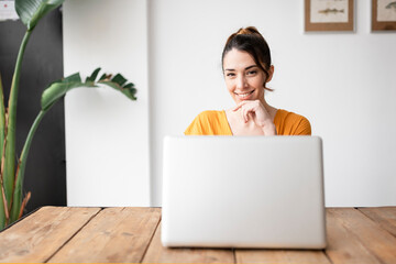 Portrait of smiling woman at home sitting at table using laptop